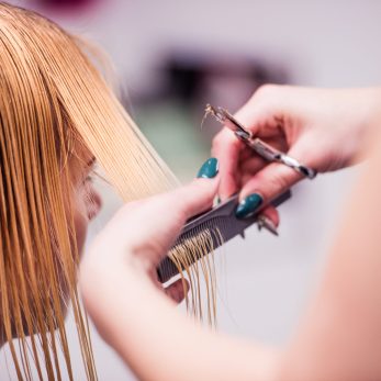 Hands of unrecognizable professional hairdresser cutting hair of her client, giving a new haircut to female customer.